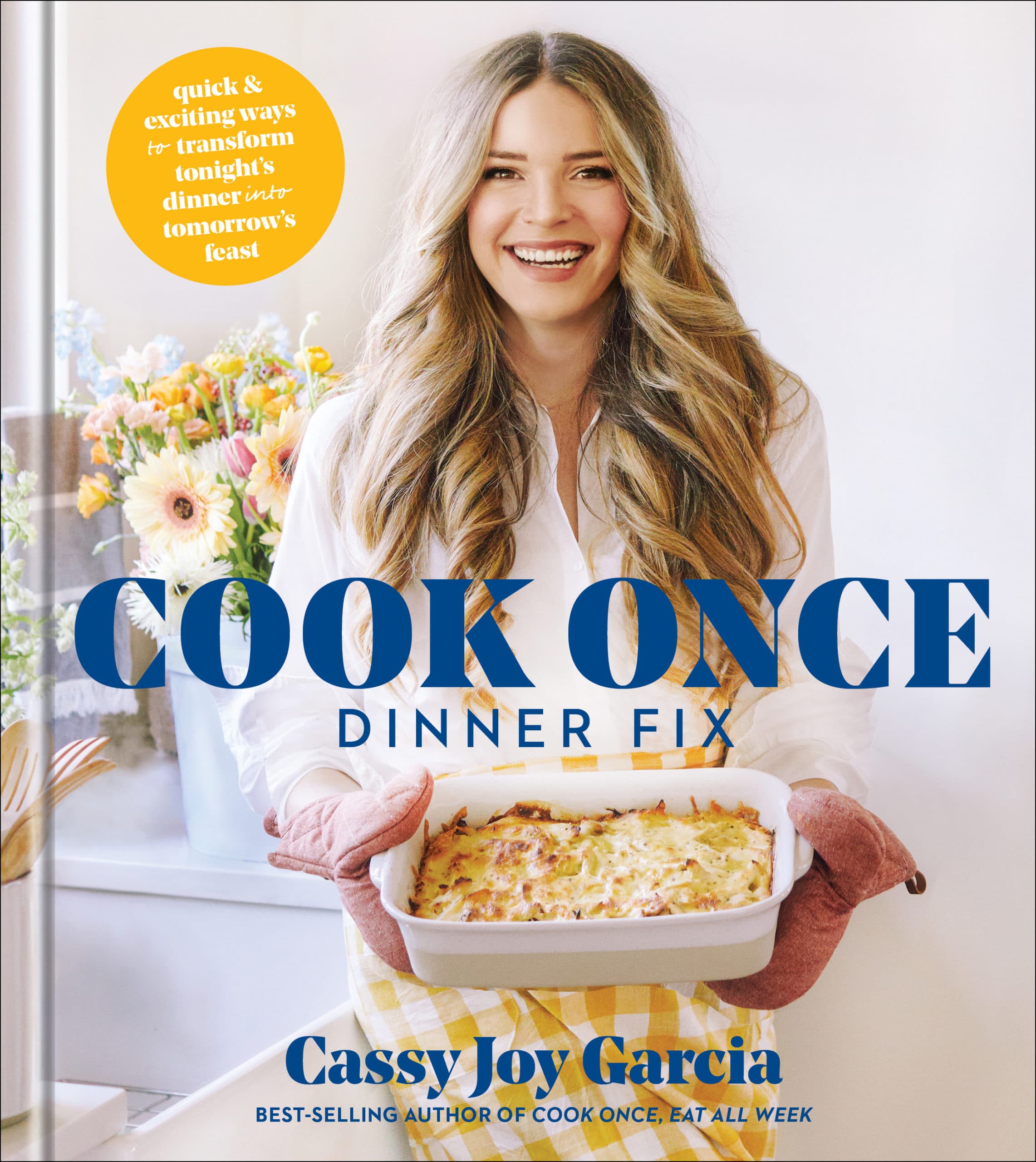 woman with brown blonde wavy hair in a white button down shirt and checkered yellow apron holding a cheesy casserole in a white dish with cook once dinner fix written on the cover